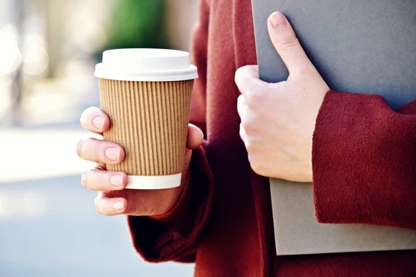 Take-away coffee seen in hand with a book. Coffee to go on a sunny day