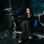 Молодая красивая белая женщина с черным вороном на руке, сидящая на диване Молодая красивая белая женщина с черным вороном на руке, сидящая на диване