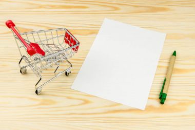 Alışveriş sepeti, kalem ve beyaz kağıt mockup ahşap arka plan kompozisyon üzerinde saçtan. Alışveriş kavramı.