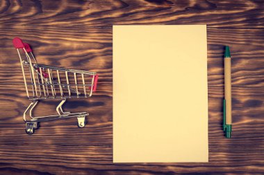 Alışveriş sepeti, kalem ve beyaz kağıt mockup ahşap arka plan kompozisyon üzerinde saçtan. Alışveriş kavramı. Tonda