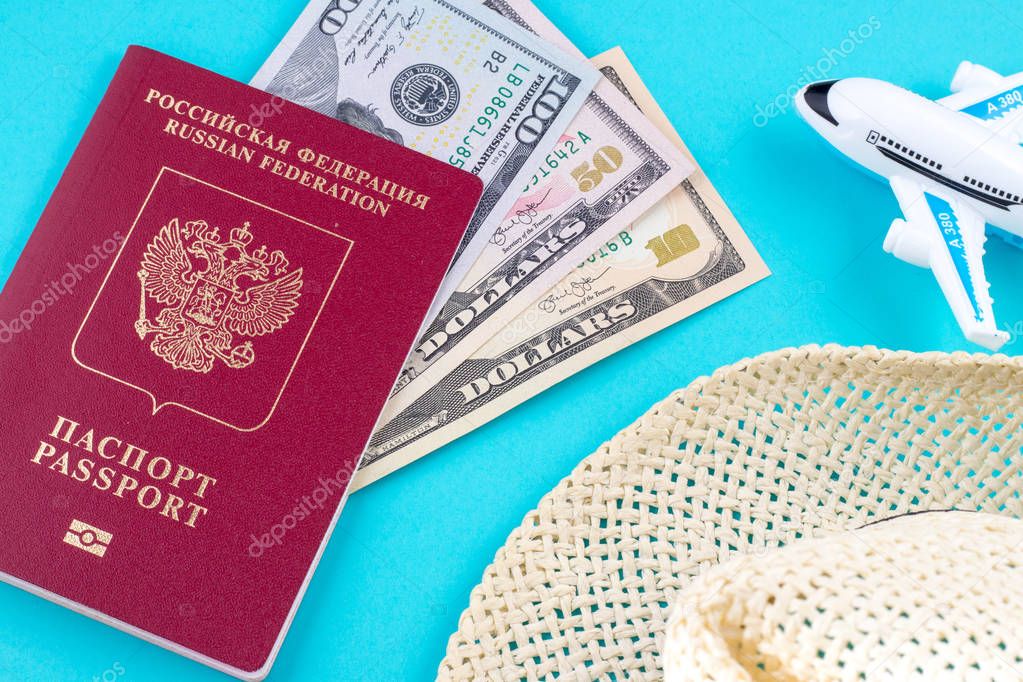 plane hat and red russian passport withdollar bills on blue background. Concept of traveling
