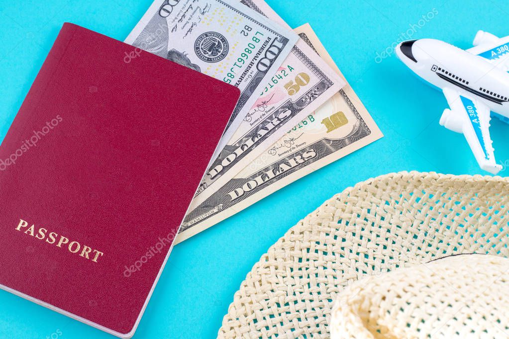plane hat and red passport withdollar bills on blue background. Concept of traveling