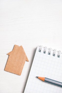 Karton ev, beyaz arka planda boş bir defter üzerindeki kalem. Dikey.