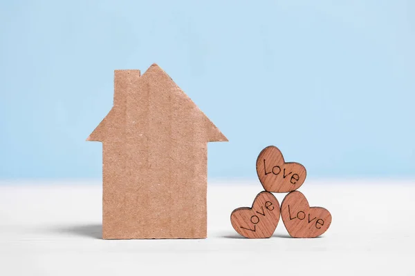 Tekturowy dom i drewniane serca z napisami Miłość na niebiesko-białym tle. — Zdjęcie stockowe