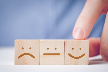 Bir adam, tarafsız ve hoşnutsuz birinin yanında pozitif bir yüzü olan tahta bir küpü işaret ediyor. Eylem veya kaynak değerlendirmesi kavramı.