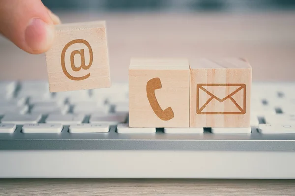 Een man houdt een houten kubus met een afbeelding van een e-mail symbool naast een telefoon en een envelop in zijn hand. Contactconcept voor communicatie. — Stockfoto