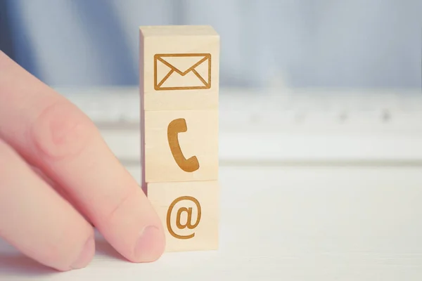 Een man houdt een houten kubus met de afbeelding van een telefoon, e-mail, letters symbool. Het concept van contacten voor communicatie, de noodzakelijke werkmethoden in het bedrijfsleven. — Stockfoto