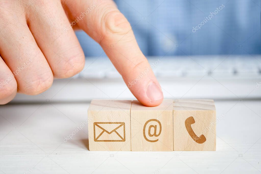 A man points to a wooden cube with the image of an email symbol next to a telephone and a letter with his hand. Contact concept for communication.