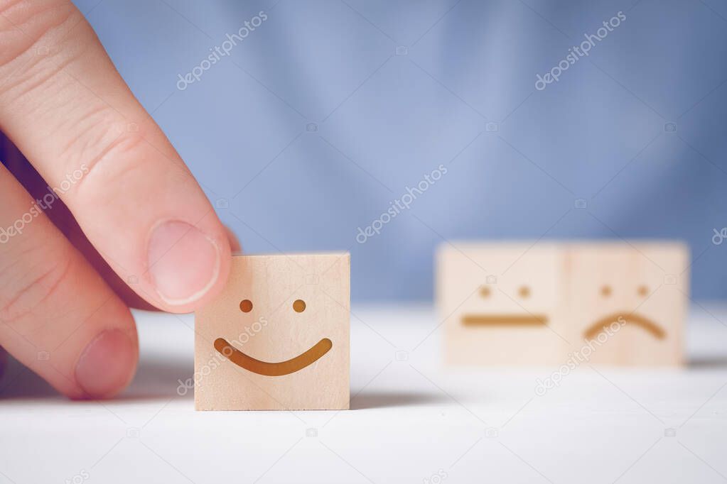 A man holds a wooden cube with a positive face on a neutral and negative background. Concept for evaluating an action or resource.