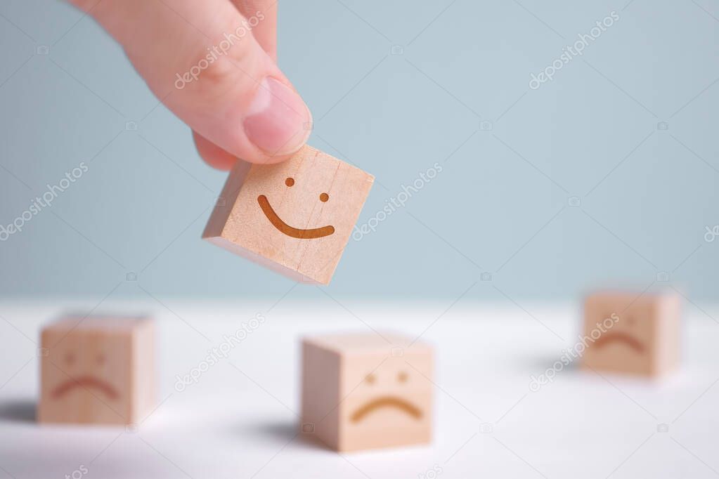 A man holds a wooden cube with a picture of a positive face on the background of negative emotions.