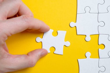 Bir soruna çözüm bulma kavramı. Yapbozun bir parçası sarı arka planda parmakları diğerlerinin yanında olan bir adam tarafından tutuluyor. Düz yatıyordu.