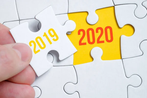 The concept of changing the year from 2019 to 2020. A piece of the puzzle is held by a man with his fingers on a yellow background.
