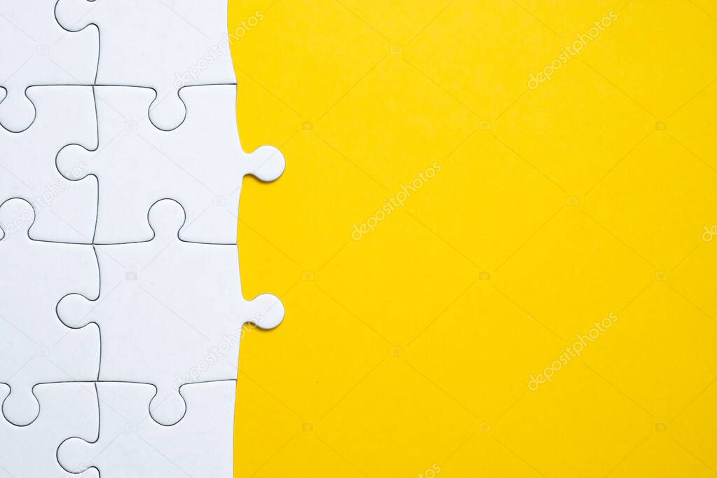 White puzzle assembled in half on a yellow background. Copy space.