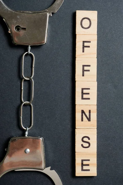 木製の文字で作られた単語は犯罪です。黒い背景の金属製の手錠。法を破るという概念. — ストック写真