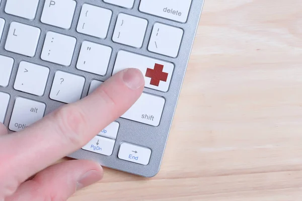 Wezwij pomoc medyczną, lekarze online. Palec naciska przycisk na klawiaturze czerwonym krzyżykiem. — Zdjęcie stockowe
