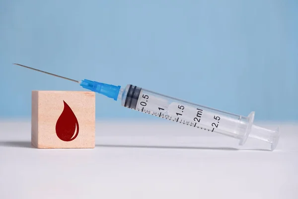 Uma seringa em um cubo de madeira com um sinal de gota. O conceito de vacinação . — Fotografia de Stock