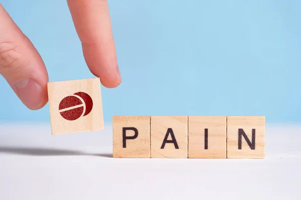 Concept application of pain pills. Fingers hold a cube with a drug icon next to the letters. — ストック写真