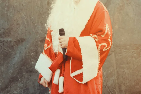 Herec oblečený jako Santa Claus vystupuje na jevišti s mikrofonem na černém pozadí. — Stock fotografie