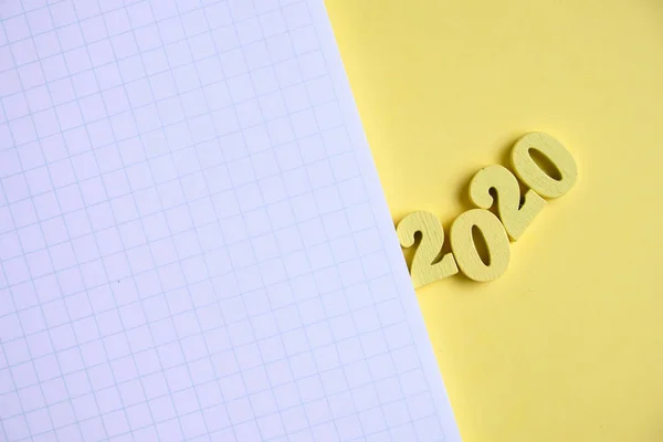 Wooden figures 2020 next to the notebook on a yellow background. Top view. Copy space. — Stock Photo, Image