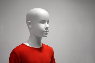 Kırmızı tişörtlü beyaz bir çocuk mankeni gri bir arkaplanda..