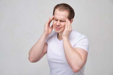 Genç adam elleriyle kafasına dokunur ve baş ağrısıyla şiddetle kaşlarını çatar..