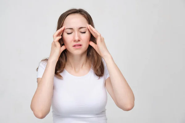 Ett porträtt av en ung flicka i vit skjorta med händerna på huvudet. Begreppet en stark huvudvärk smärta. huvudvärk. — Stockfoto