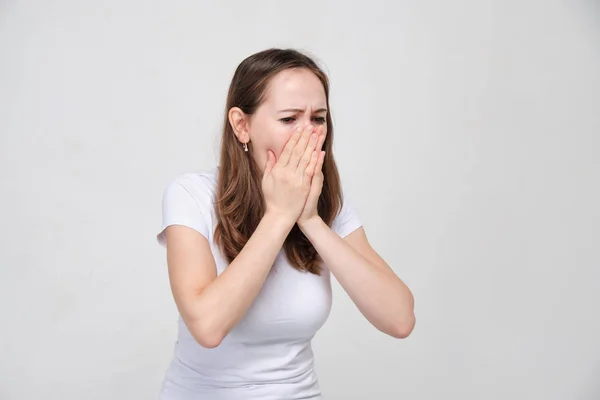 Ett porträtt av en ung flicka i en vit skjorta händer skär munnen av hosta. Begreppet halsont och förkylning och influensa. — Stockfoto