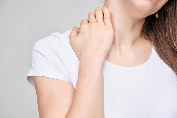 Uma menina em uma camiseta branca toca seu pescoço com a mão por causa da dor intensa . — Fotografia de Stock