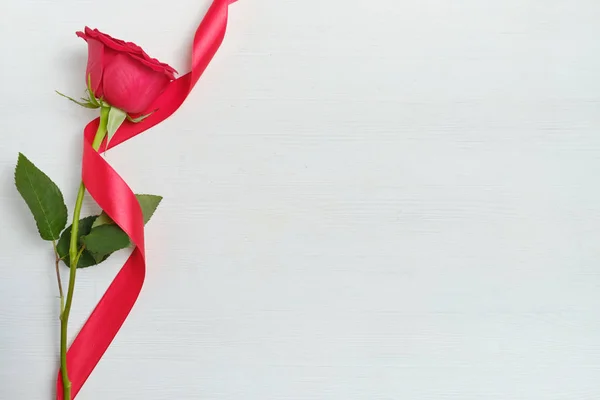 Una hermosa rosa roja con una cinta sobre un fondo de madera blanca. Vista superior. Copiar espacio . — Foto de Stock