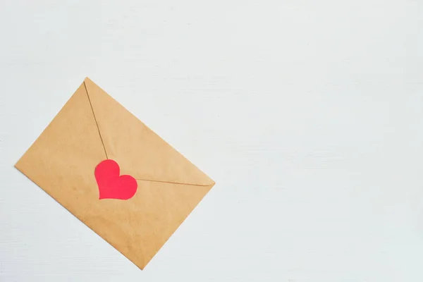 Rood hart met een ambachtelijke envelop op een witte houten achtergrond. Kopieerruimte. — Stockfoto