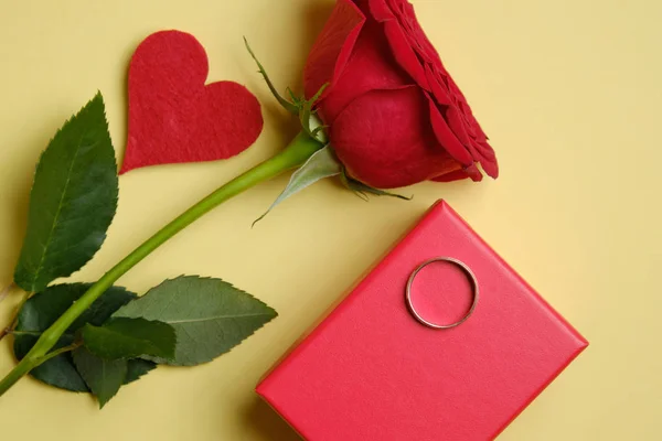 Caja roja con un anillo de oro cerca de una rosa sobre fondo amarillo . — Foto de Stock