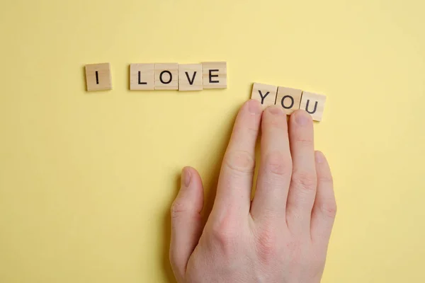 The word - I love you - from wooden squares on a yellow background. The hand moves the figures. — ストック写真