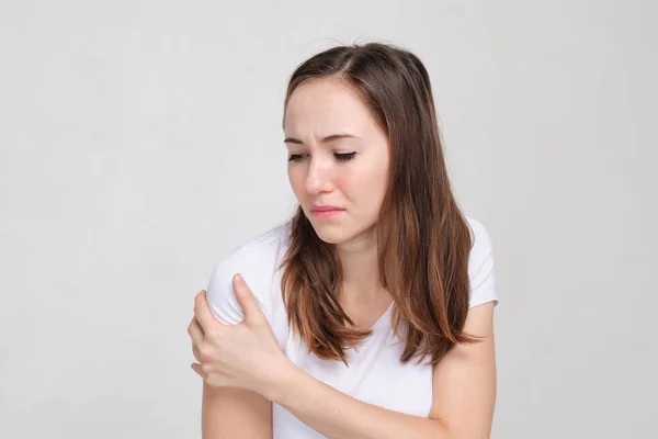 A girl in a white T-shirt oils her shoulder with her hand. The concept of muscle pain. — Stock Photo, Image