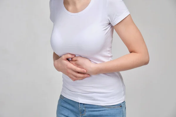 A girl in a white T-shirt massages her stomach with her hands. Belly pain. The concept of poisoning. Muscle spasm.