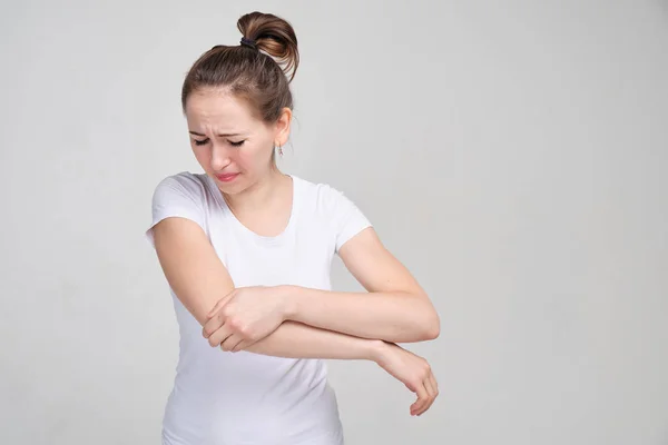 En tjej i vit T-shirt masserar armbågen med handen. Begreppet blåmärken, smärta, ligament. — Stockfoto