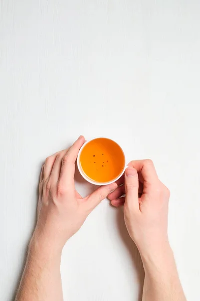 Tangan memegang secangkir teh segar pada latar belakang kayu putih . — Stok Foto