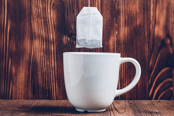 A white cup of tea with a tea bag above it against the background of a burnt board. — 스톡 사진