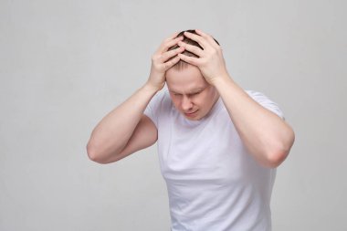 A man in a white T-shirt suffers from headaches and migraines.