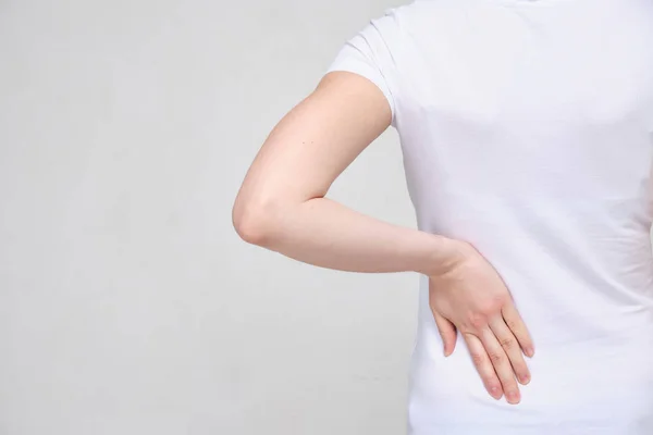 Ένα κορίτσι με λευκό μπλουζάκι υποφέρει από πόνο στο κάτω μέρος της πλάτης. Έννοια Sciatica. — Φωτογραφία Αρχείου