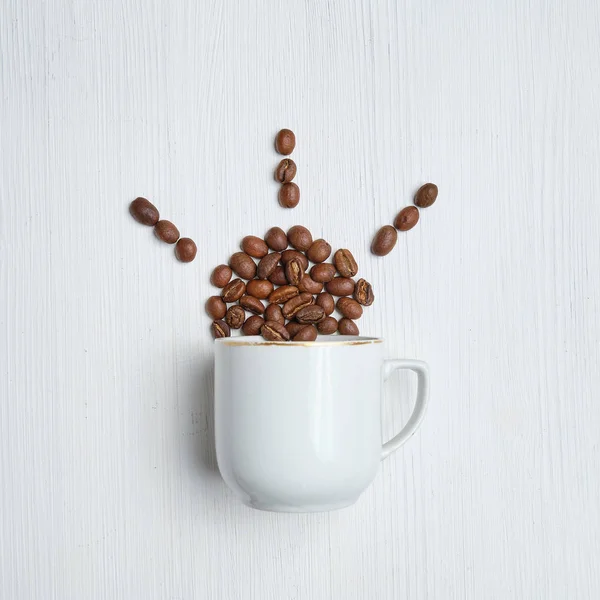 Sol abstracto hecho de granos de café y una taza blanca sobre un fondo de madera . — Foto de Stock
