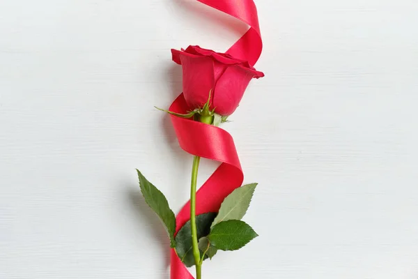 Una hermosa rosa roja con una cinta sobre un fondo de madera blanca. Vista superior . — Foto de Stock