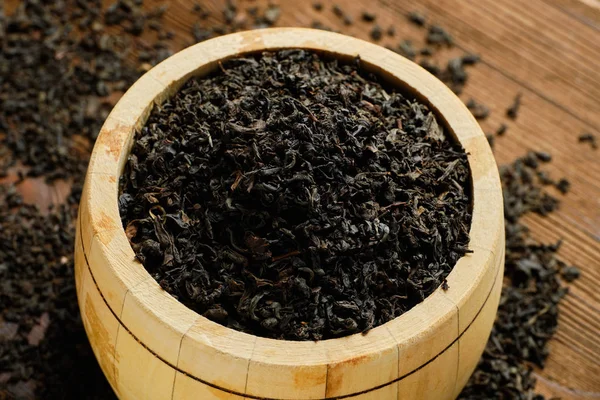 Black tea in barrel and scattered tea on wooden background. View from top. — 图库照片