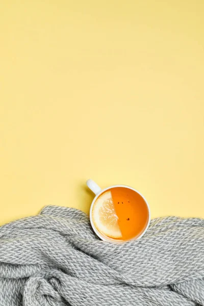 Secangkir teh hitam dengan irisan lemon, syal abu-abu dengan latar belakang kuning . — Stok Foto