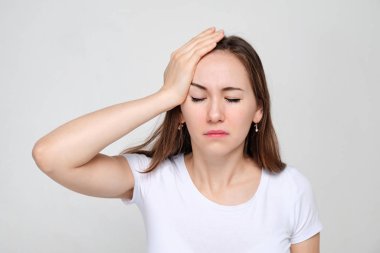 The girl in the white T-shirt holding hand to head suffers from forgetfulness. Memory problems.