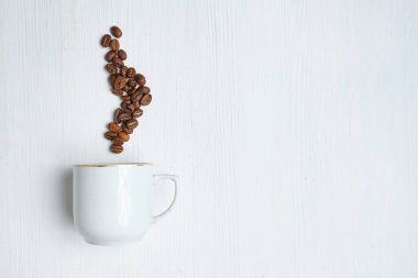 White cup with abstract steam from coffee beans on a white wooden background.