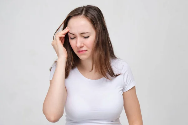 A girl in a white T-shirt rubs her forehead and tries to remember the event. — Stockfoto
