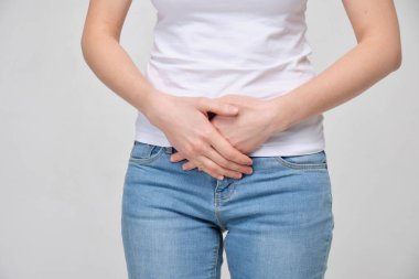 A girl in a white T-shirt massages the lower abdomen.