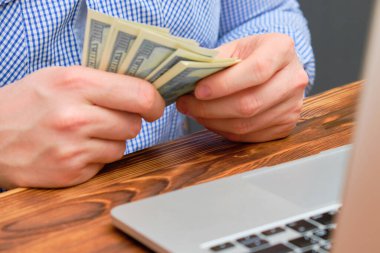 A man counts profit in the form of money from the business in front of the laptop.