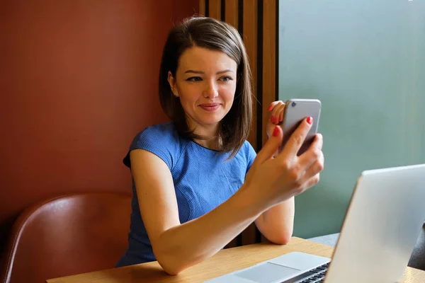 Μια γυναίκα κάθεται σε ένα καφέ μπροστά από ένα φορητό υπολογιστή και κάνει μια βιντεοκλήση και επικοινωνεί. — Φωτογραφία Αρχείου