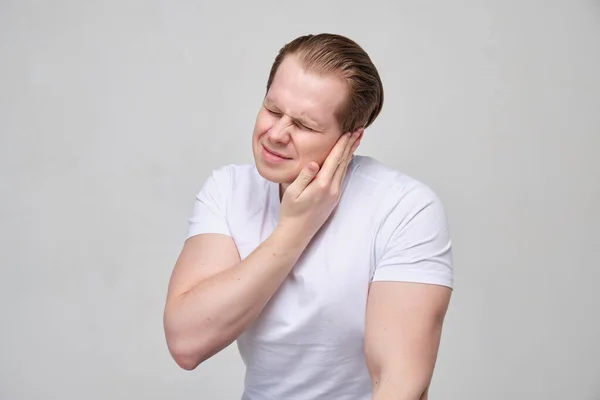 Чоловік з білою футболкою масажує вухо болем . — стокове фото